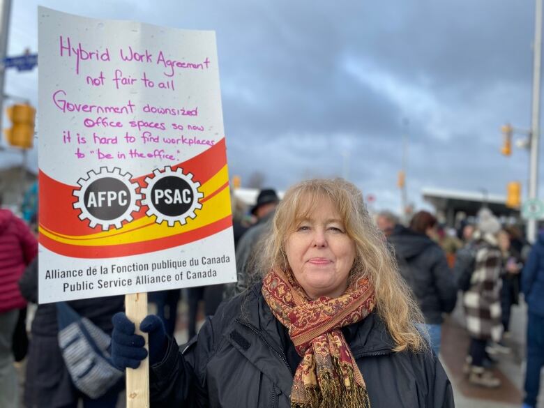 Someone holds a sign at a protest with a long message about the challenges of working in the office.