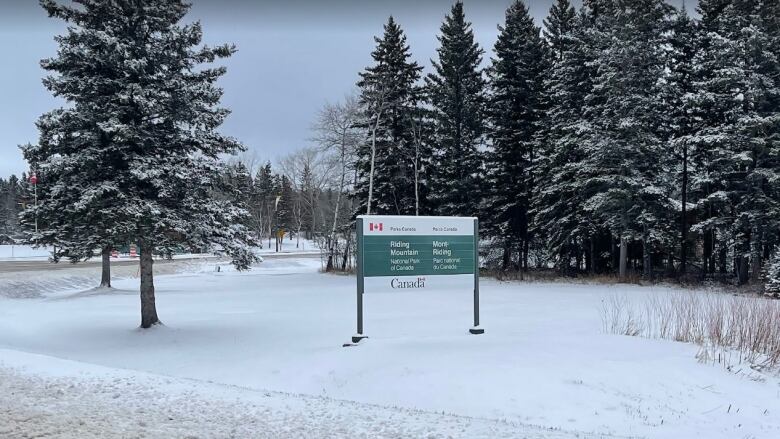 Snow is seen by a sign for Riding Mountain National Park.