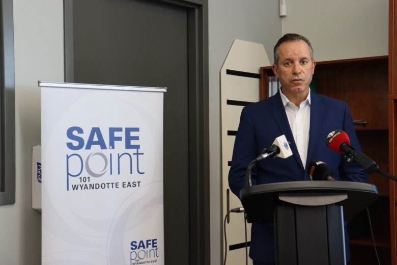 A man in a blue suit stands behind a podium next to a banner reading 