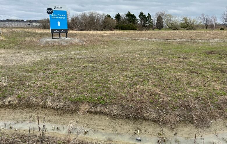 open field as seen in April with a stream in the foreground and a blue sign in the middle