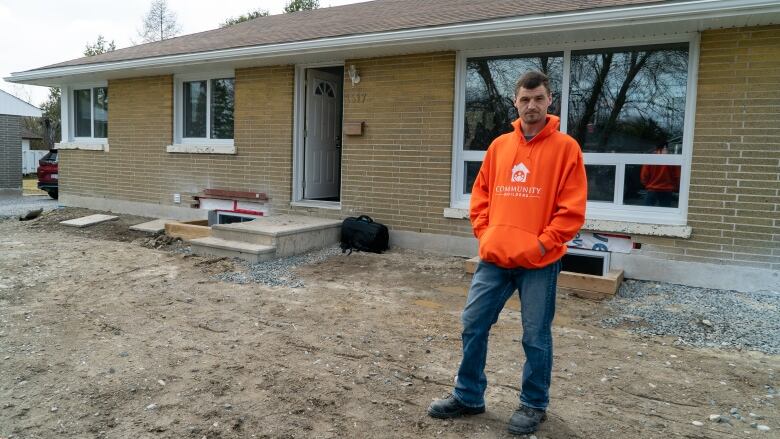 A man in an orange hoodie standing outside a house.