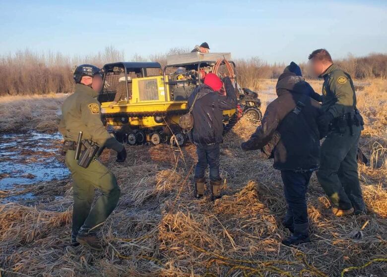 A tracked rescue vehicle anf agents and migrants in a flooded field.