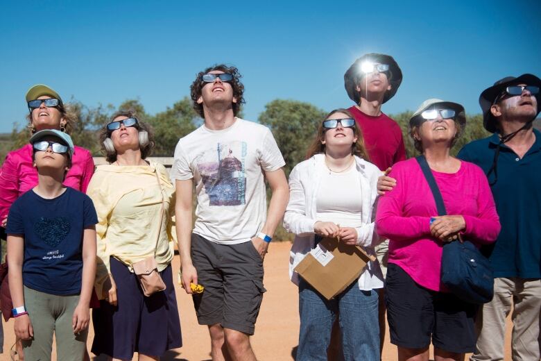 Several people wearing special glasses look skyward.