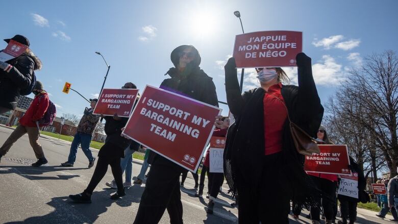 Striking workers carry signs while the sun glares behind them.