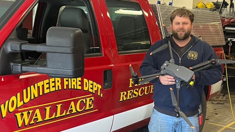 A man holds a drone while standing next to a fire truck.