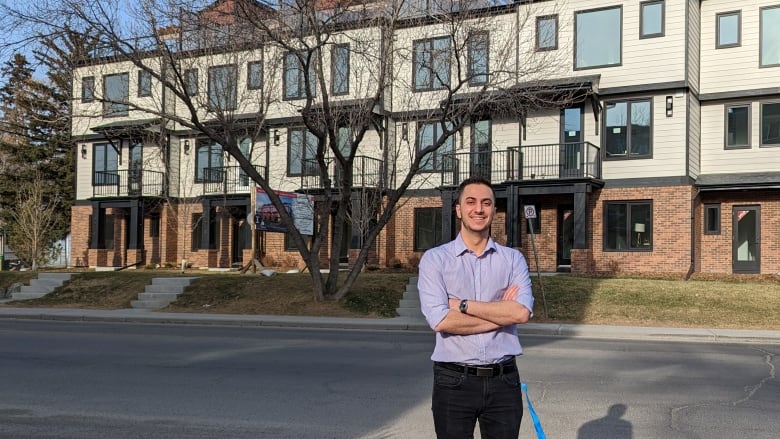 A man in his 20s stands in front of a stretch of row housing. 