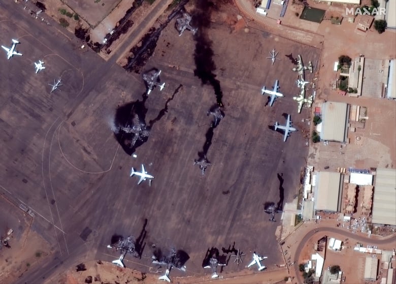 Black smoke billows from airplanes on a tarmac, as seen from above.