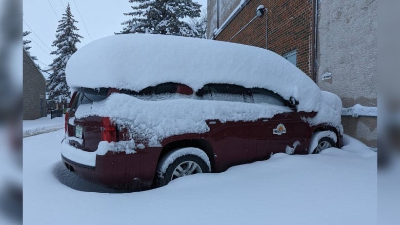 A red van is covered in piles of snow. 