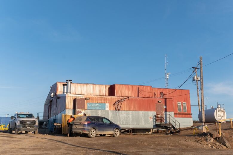 Red and grey building on dirt, two trucks.