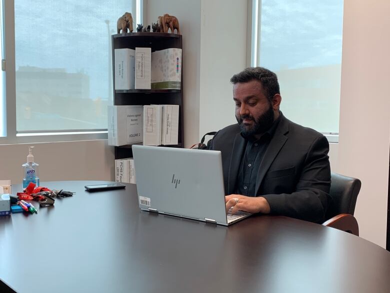 Amanjit Kahlon sits in a chair with his laptop placed on top of a table, typing away. 