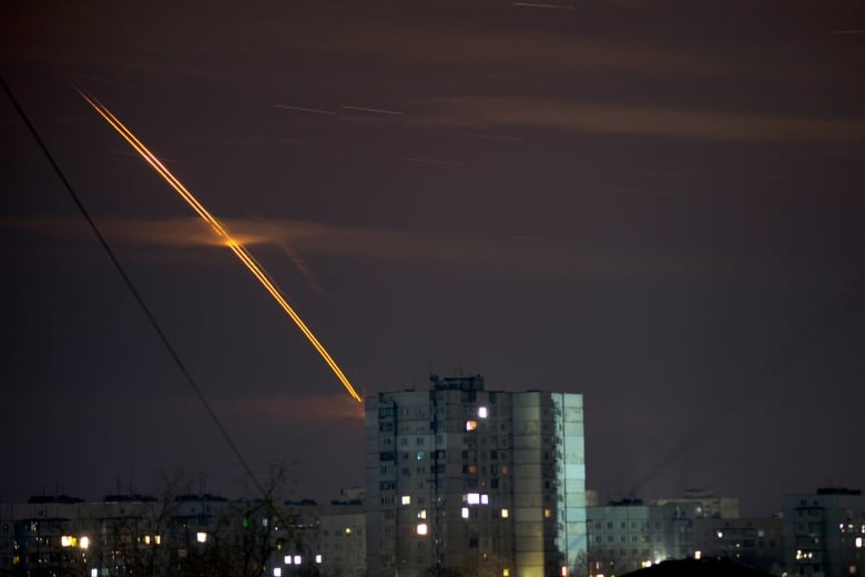 A bright trail is shown in the sky above an urban landscape at night.