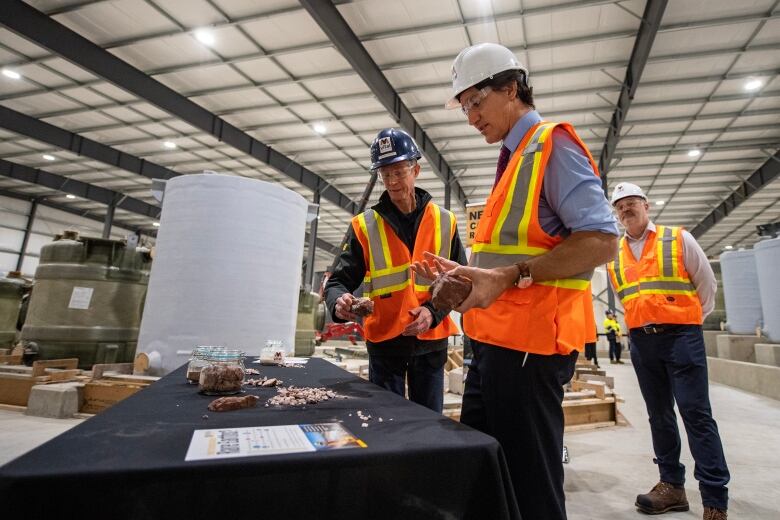 3 men in  construction vests. Canada's prime minister is holding a critical mineral while speaking to another man. 