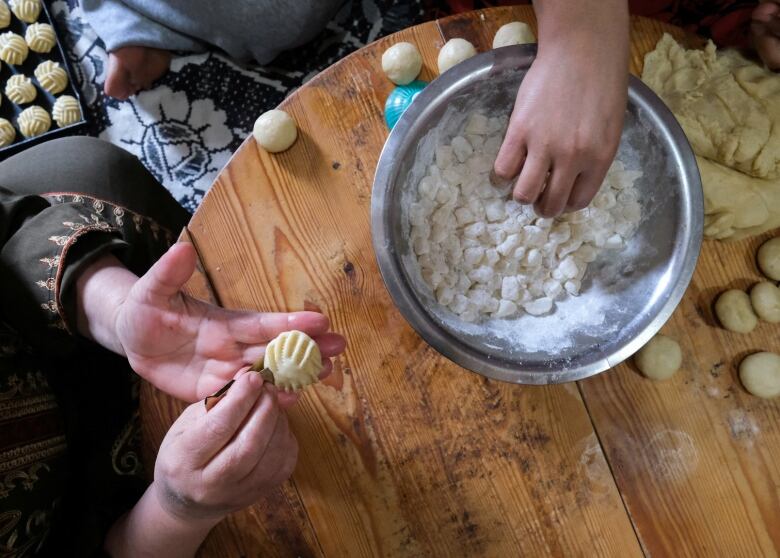 View from above of hands of two women making traditional Egyptian butter cookies called 'Kahk' at a table that shows a medal bowl and lots of rolled dough.