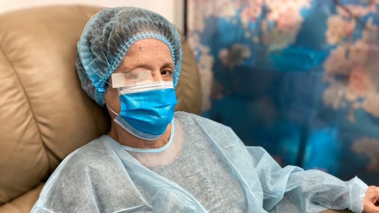 A woman with a patch over one eye, wearing a surgical gown and cap over her head.