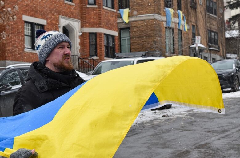 A man stands in the snow holding a Ukrainian flag, looking upwards.