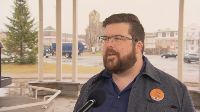 A bearded man with glasses speaking with a microphone in front of him.