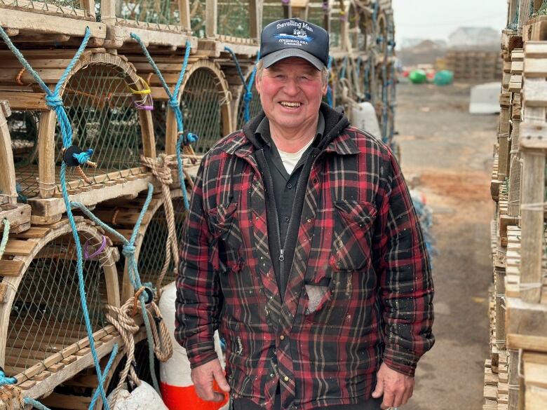 A man in a plaid shirt and ballcap stands in front of lobster traps 