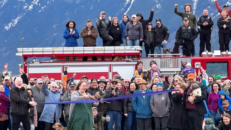 Photo shows people with their hands in the air, cheering while a woman cuts a ribbon. 