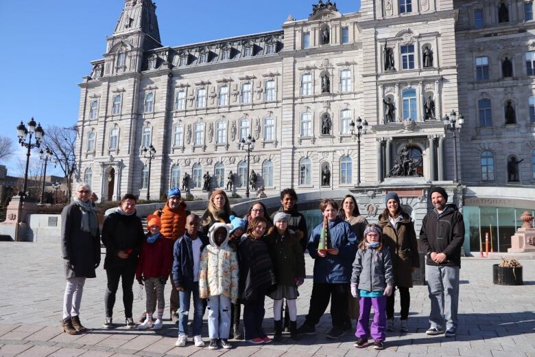 A group of people in coats stand outside the National Assembly in Quebec City