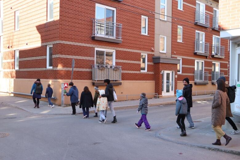 A group of people walk across the street. Adults hold the hands of children. 