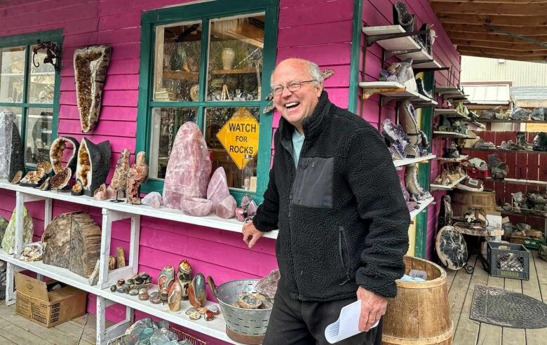 Photo shows a man laughing, standing in front of a rock shop. 