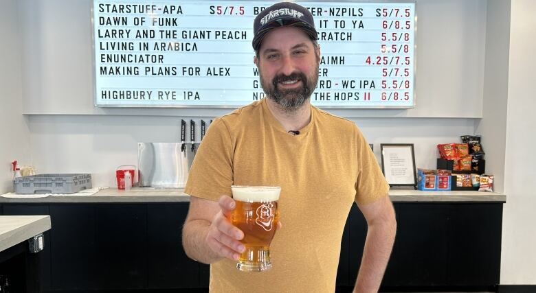 A man is pictured holding a cup of beer towards the camera.