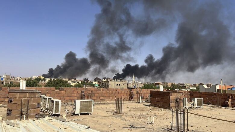 Black smoke rises from a cityscape in the distance.