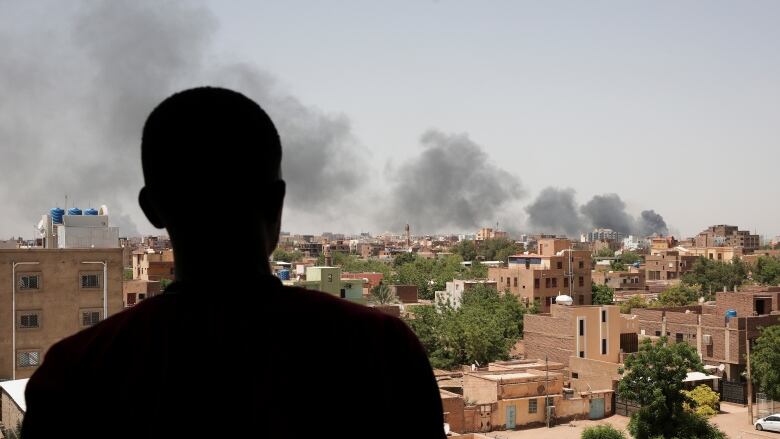 A person looks at a plume of smoke rising over a city.