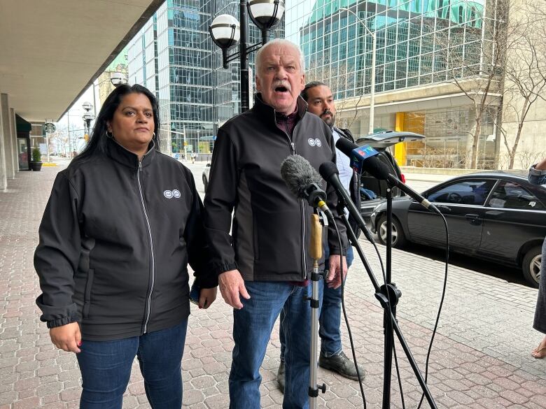 Two men and a woman talk in front of microphones.