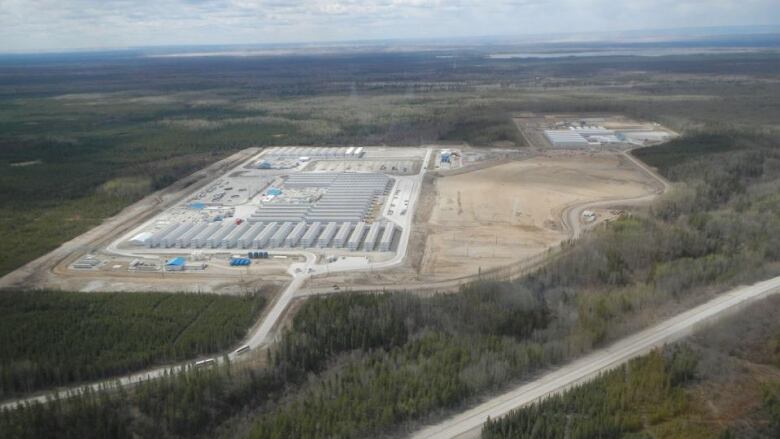 An aerial image of the camp amid the forests of northern Alberta. The camps has numerous rows of while accommodation buildings. 