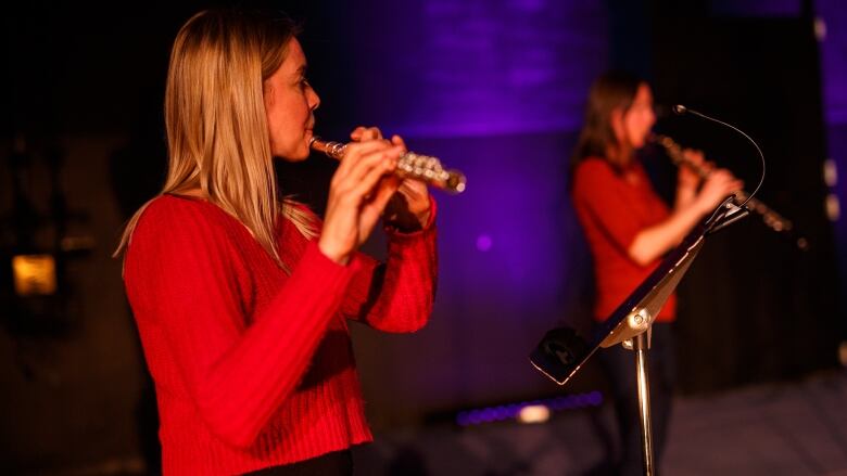 A woman in a red sweater plays the flute. 