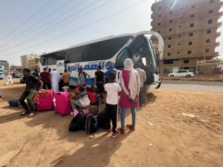 A group of people gather around and load their bags onto a coach bus.