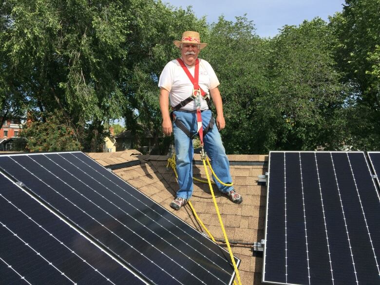 Andrew Mills stands on the roof of a house between two solar panels.