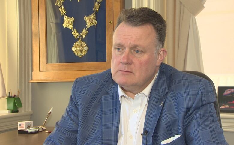 A man in a suit jacket sits at a desk.