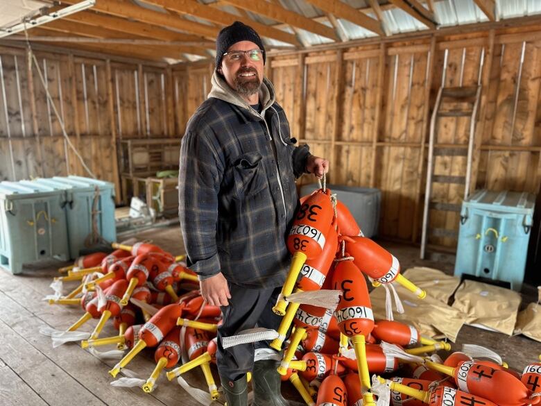 A man in a plaid jacket and toque holds strings full of plastic buoys 