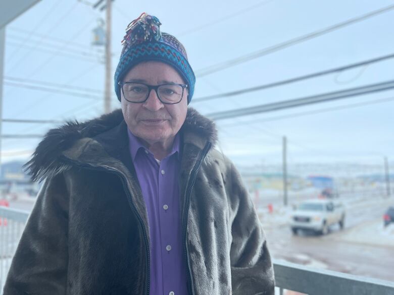 A man in a knitted multicoloured toque and seal skin jacket, stands expressionless for a photograph.