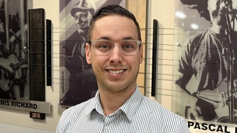 A man with glasses smiles in front of artwork on the wall behind him.