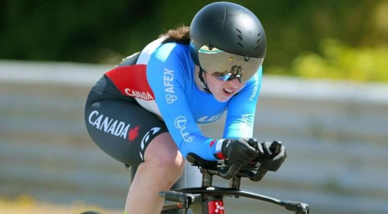 A helmeted competitive female cyclist is down in her aerobars in a time-trial position.