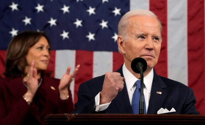 A man and a woman are shown in front of an American flag.