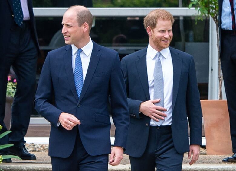 Two men in blue suits walk outside.