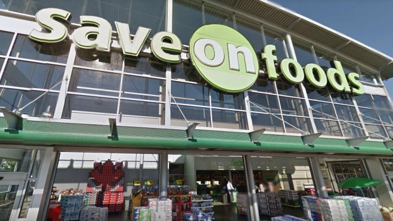 A large glass building fronted by a wide open entryway with a large sign above it that says 'save on foods' in white and green.