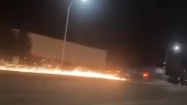 Sparks shoot up from the ground as a blurry truck drives down a highway.