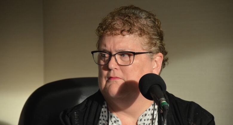 A woman wearing glasses sits in front of a microphone.