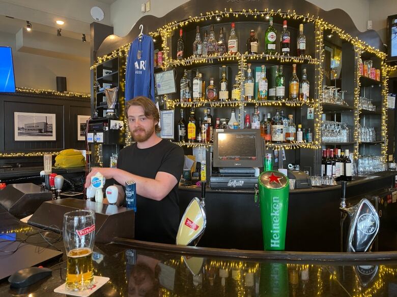 A blond man in a black shirt behind the bar pours a draft beer from the tap.