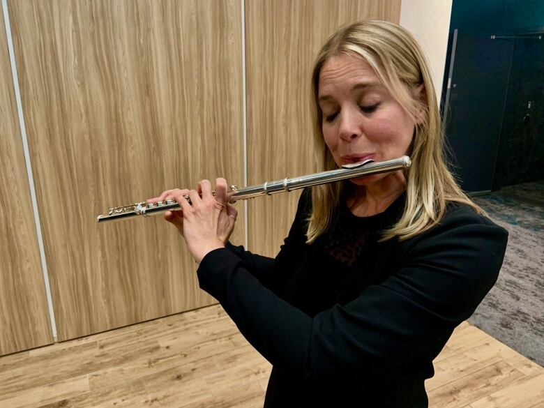 Woman in black plays the flute. 