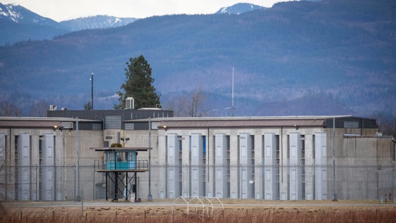 A concrete prison with a blue watch tower in front of it. In the distance are many mountains. 