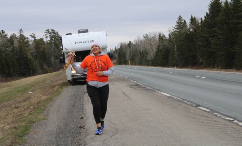 An Indigenous women runs along side the highway with a baton and orange shirt. 