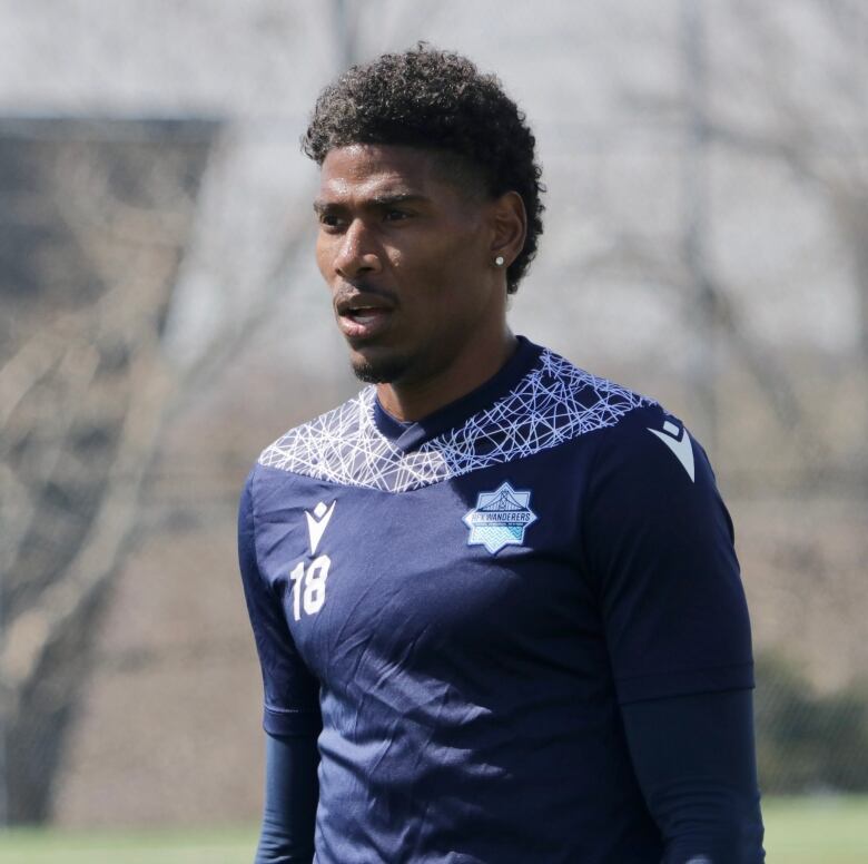 A man wearing a soccer uniform stands still on the pitch. 