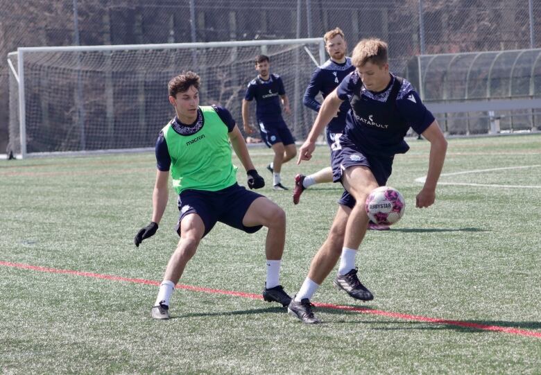 Two soccer players battle for the ball on a soccer pitch.