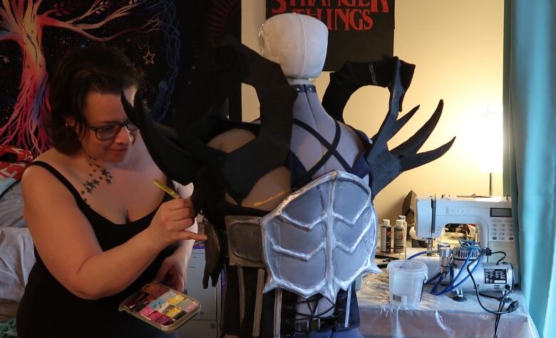 A woman paints a piece of armour on a costume.